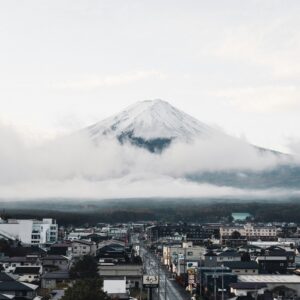 A captivating view of Mount Fuji surrounded by clouds, towering over a Japanese town with clear skies.