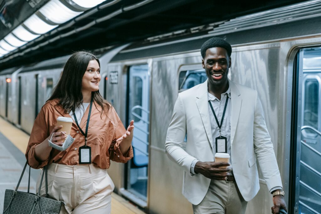 Two professionals conversing and holding coffee at an urban subway platform.